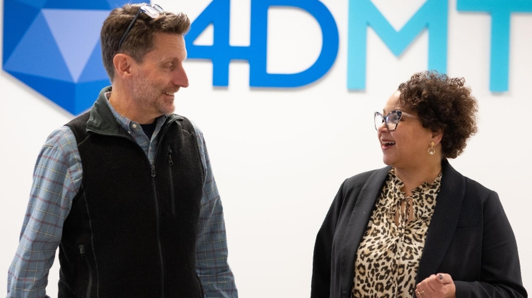 Two 4DMT colleagues talking together in front of the company sign