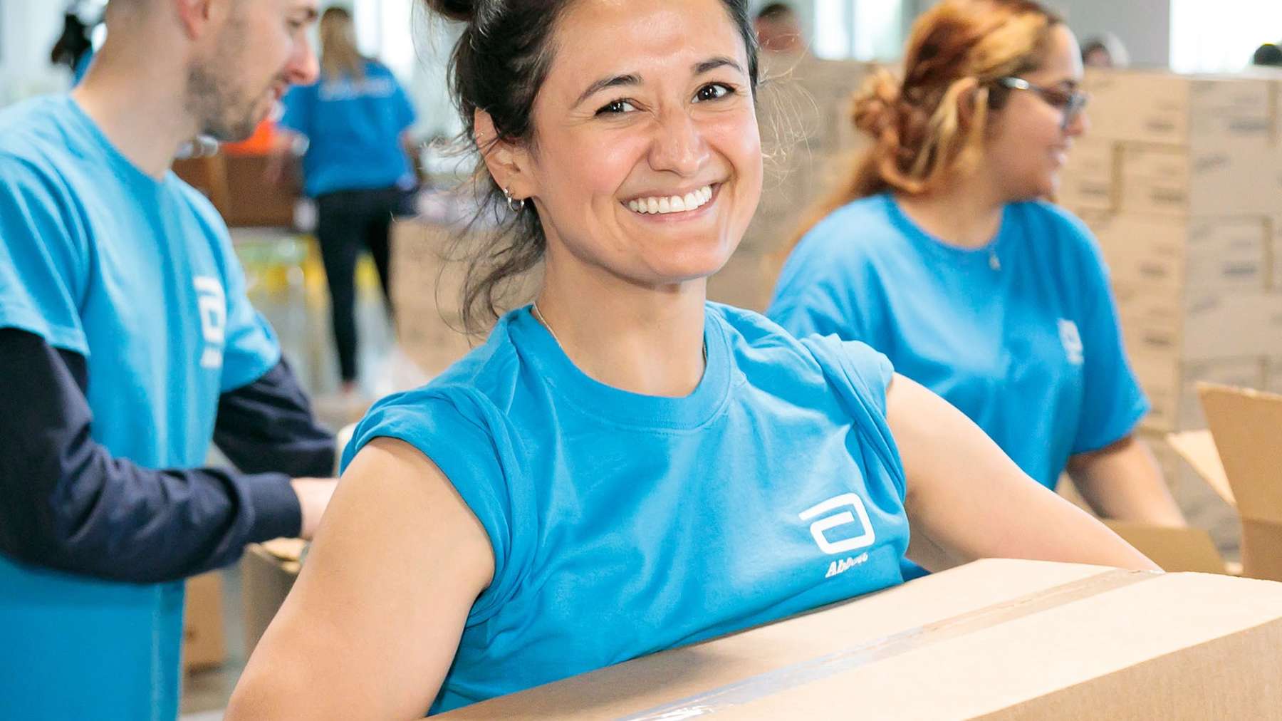 Smiling Abbott colleagues in Abbott T-shirts packing disaster relief boxes together