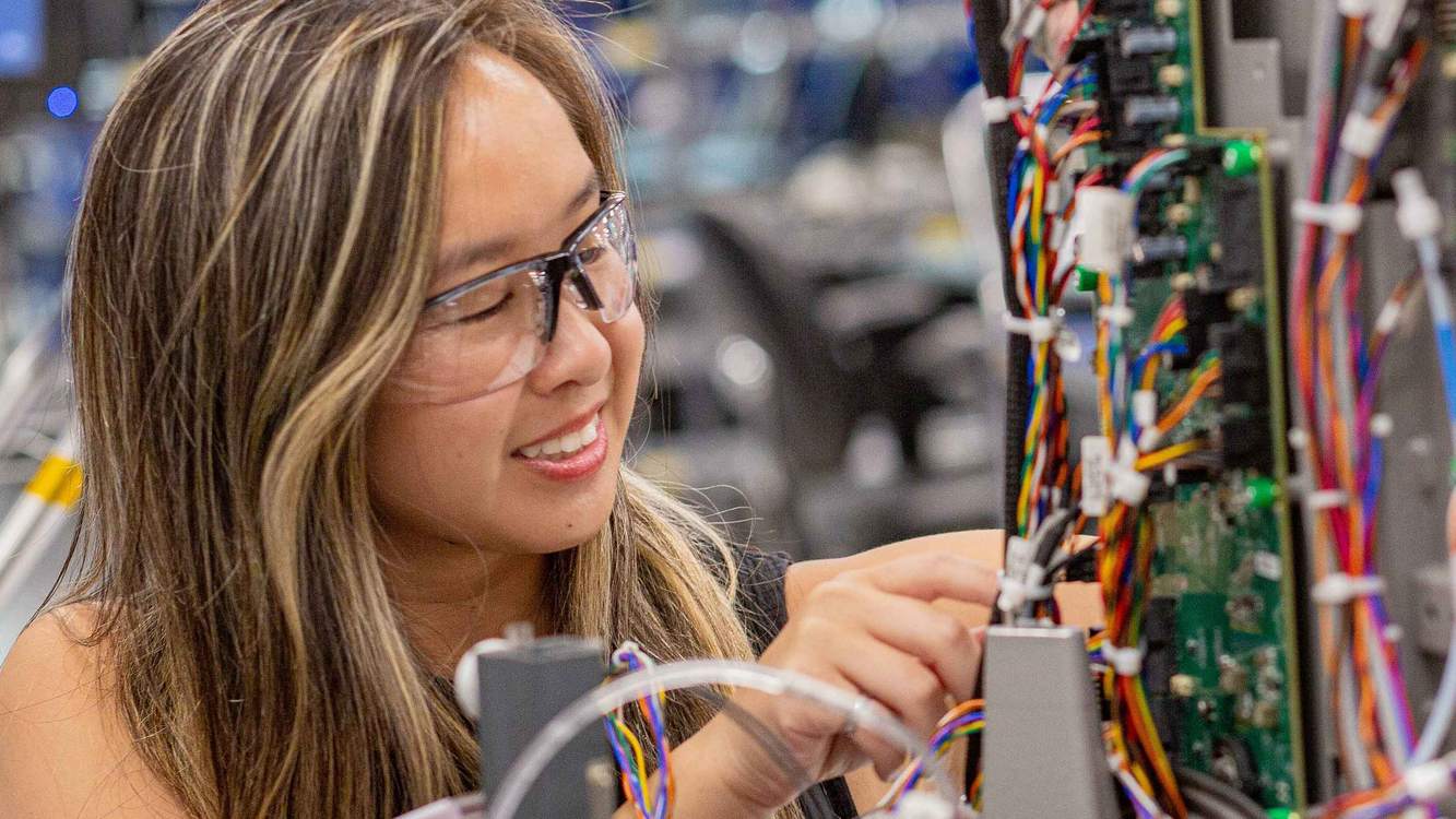 A smiling Abbott engineer in safety glasses working on the wiring inside an instrument