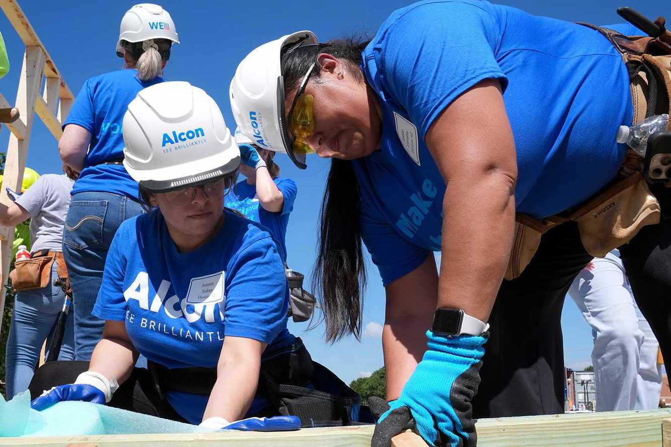 Alcon volunteers in Alcon hard hats and blue shirts building a timber frame at a Habitat for Humanity build
