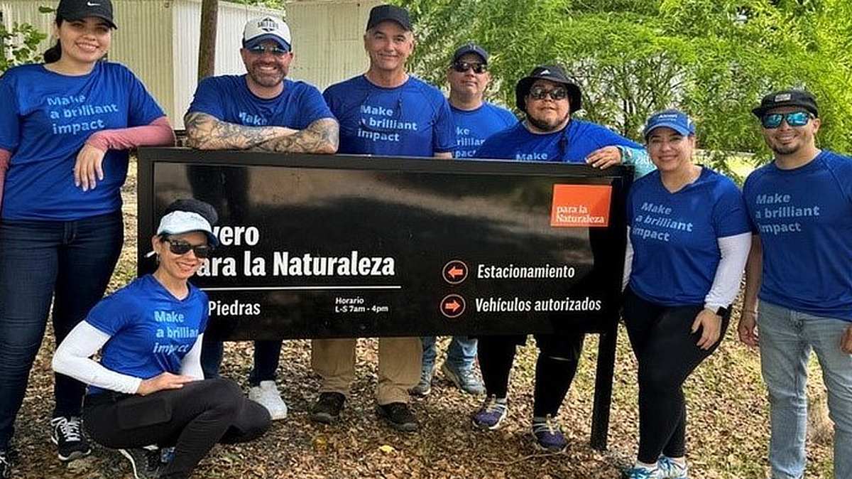About a dozen smiling Alcon volunteers in blue shirts gathered around a park sign in Puerto Rico