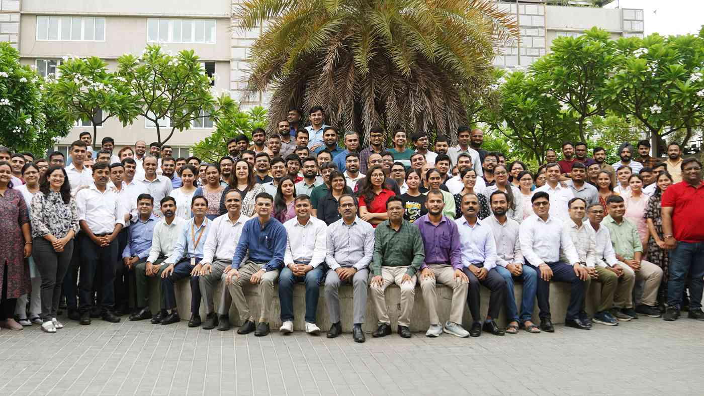 A large group of smiling Amneal colleagues in India gathered for a team photo under a palm tree