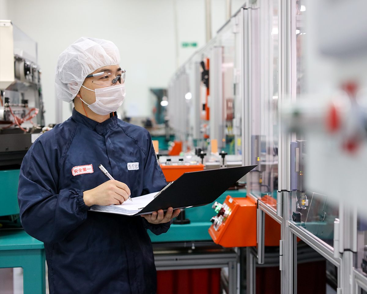 A BD manufacturing associate in cleanroom clothing and a hair cover recording a check on a clipboard beside production equipment