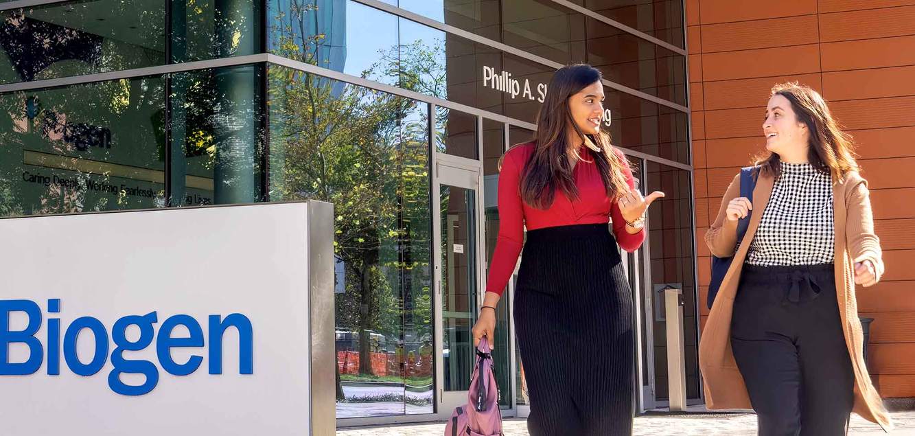Two Biogen colleagues walking past the Biogen sign outside the company's offices