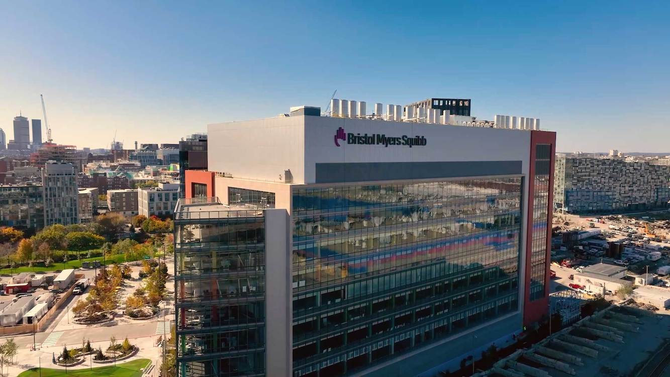 Bristol Myers Squibb's glass research building at Cambridge Crossing with the Boston skyline behind it