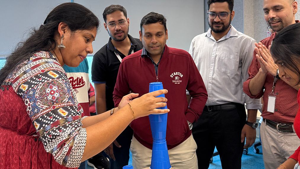 A team of smiling Bristol Myers Squibb colleagues cheering as a coworker stacks cups in an office game