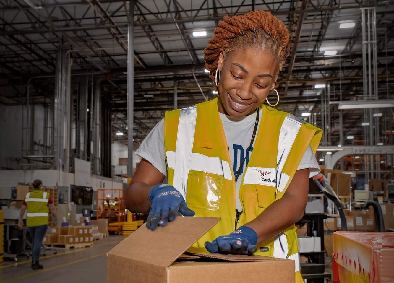 A smiling Cardinal Health associate in a safety vest packing an order in a distribution center