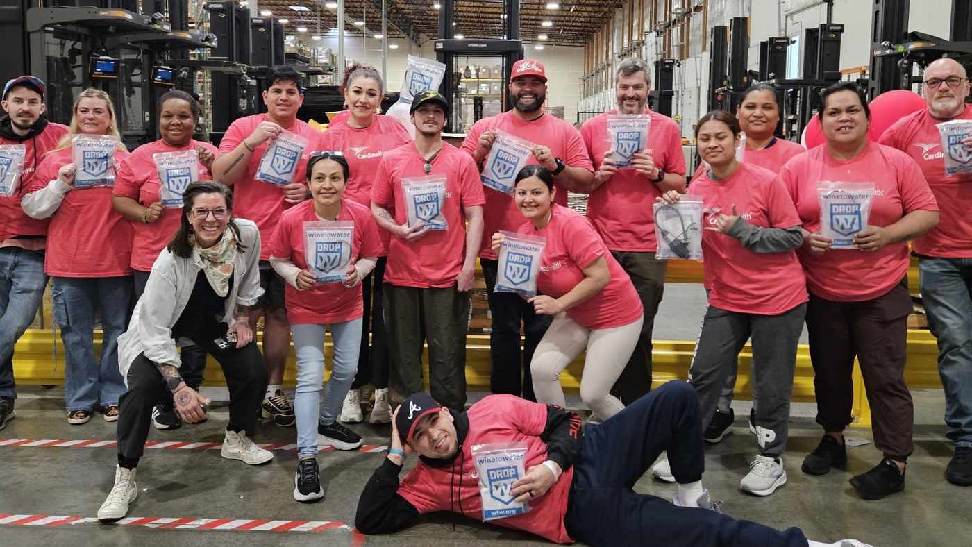 More than twenty smiling Cardinal Health colleagues in matching pink shirts posing in their Portland warehouse