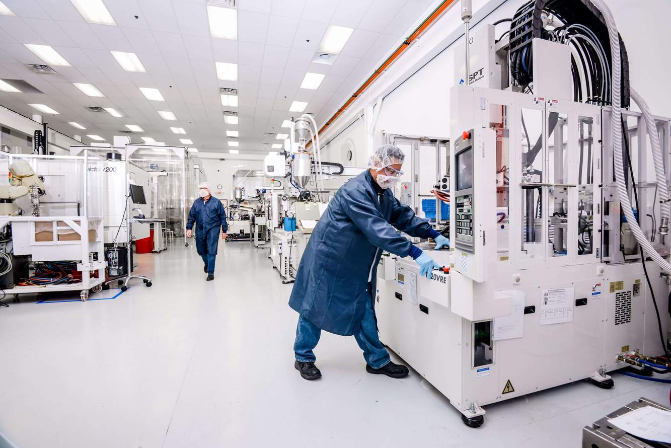A Cretex Medical operator in a blue cleanroom coat running an injection molding press on a bright production floor