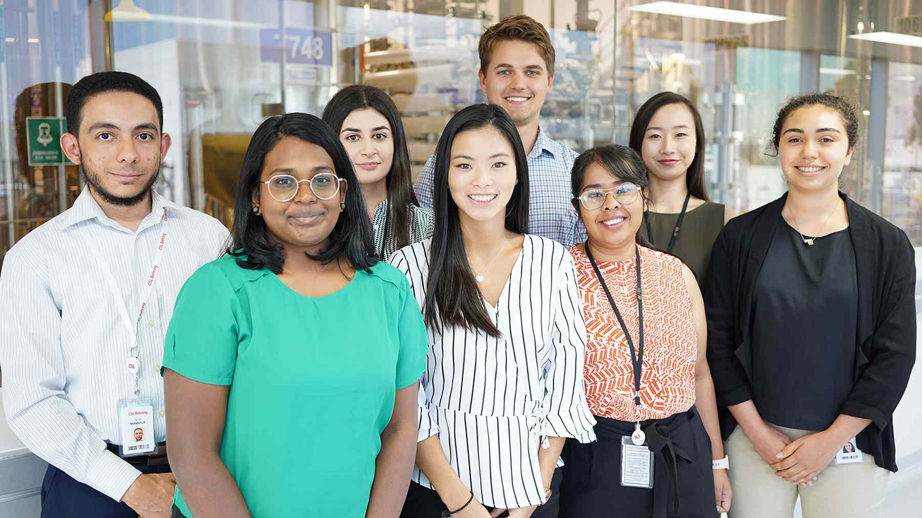 Nine smiling members of CSL's graduate program standing together in an office atrium