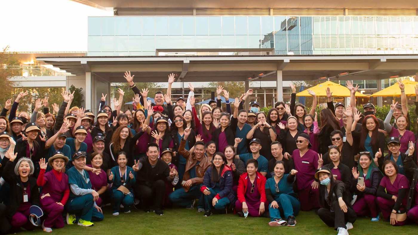 More than a hundred smiling Edwards colleagues waving together on a lawn outside the Irvine campus