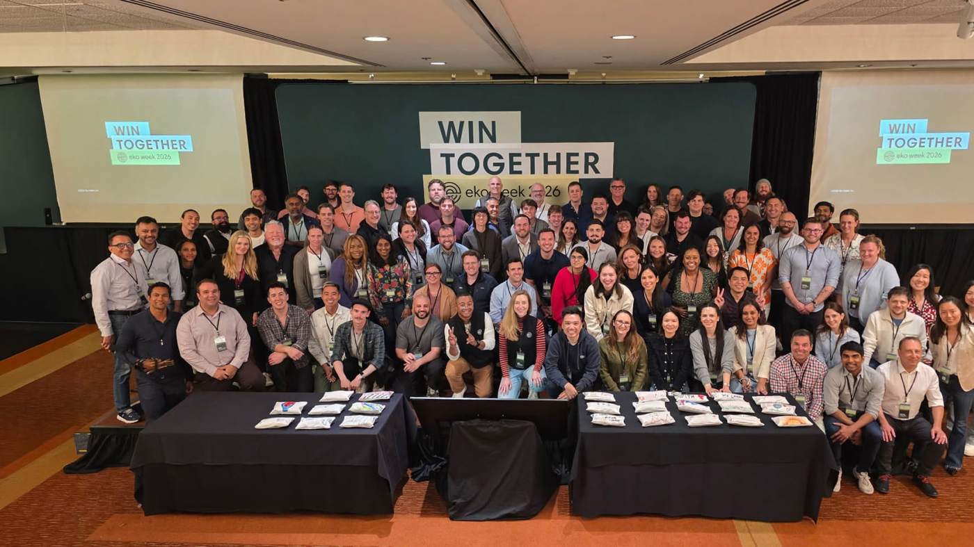 About a hundred smiling Eko colleagues gathered in front of a Win Together banner at a company event