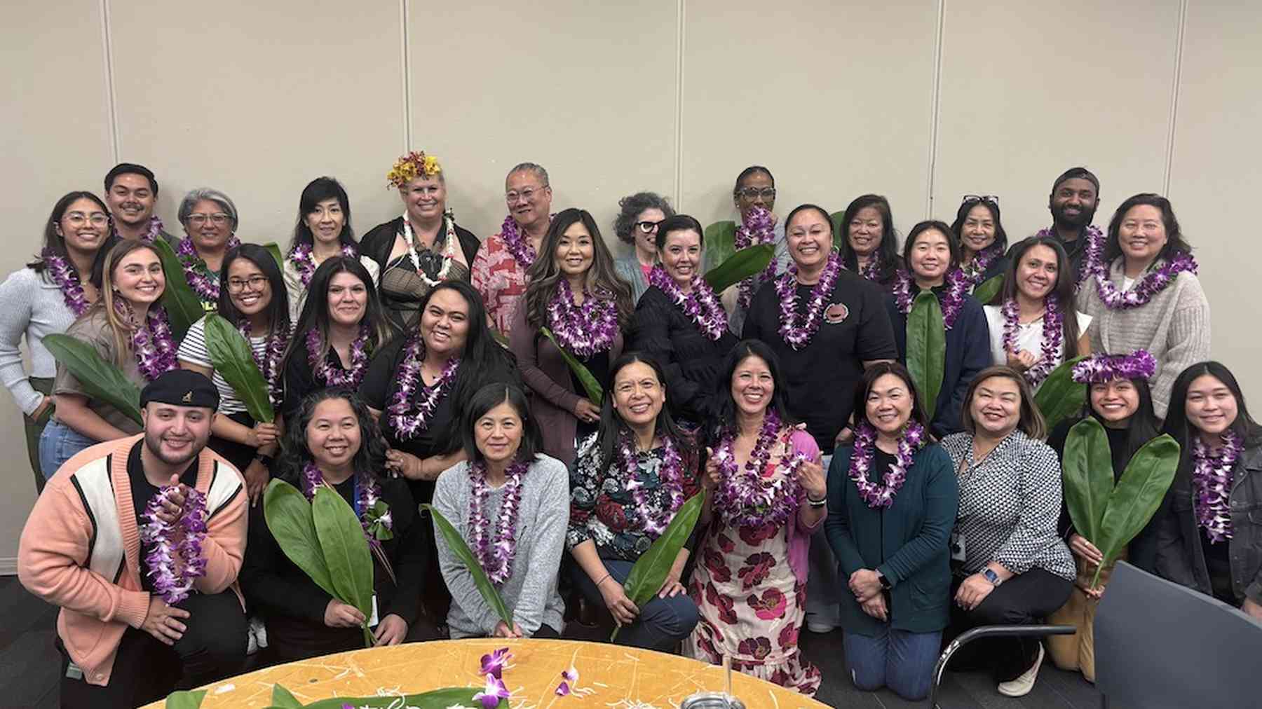 About thirty smiling Genentech colleagues wearing flower leis, gathered together at an employee resource group event