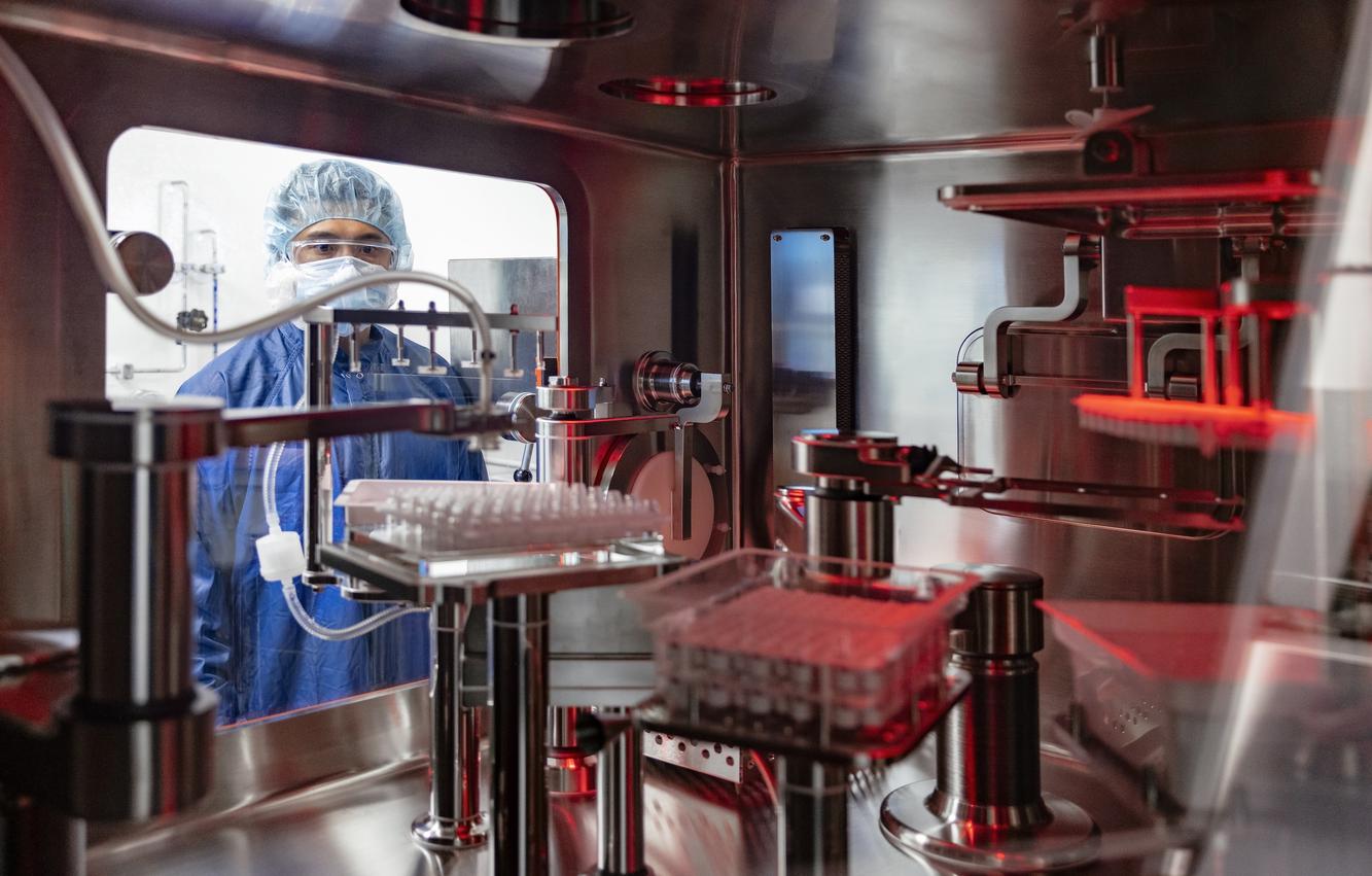 A Genentech operator in a hairnet working at an automated manufacturing isolator