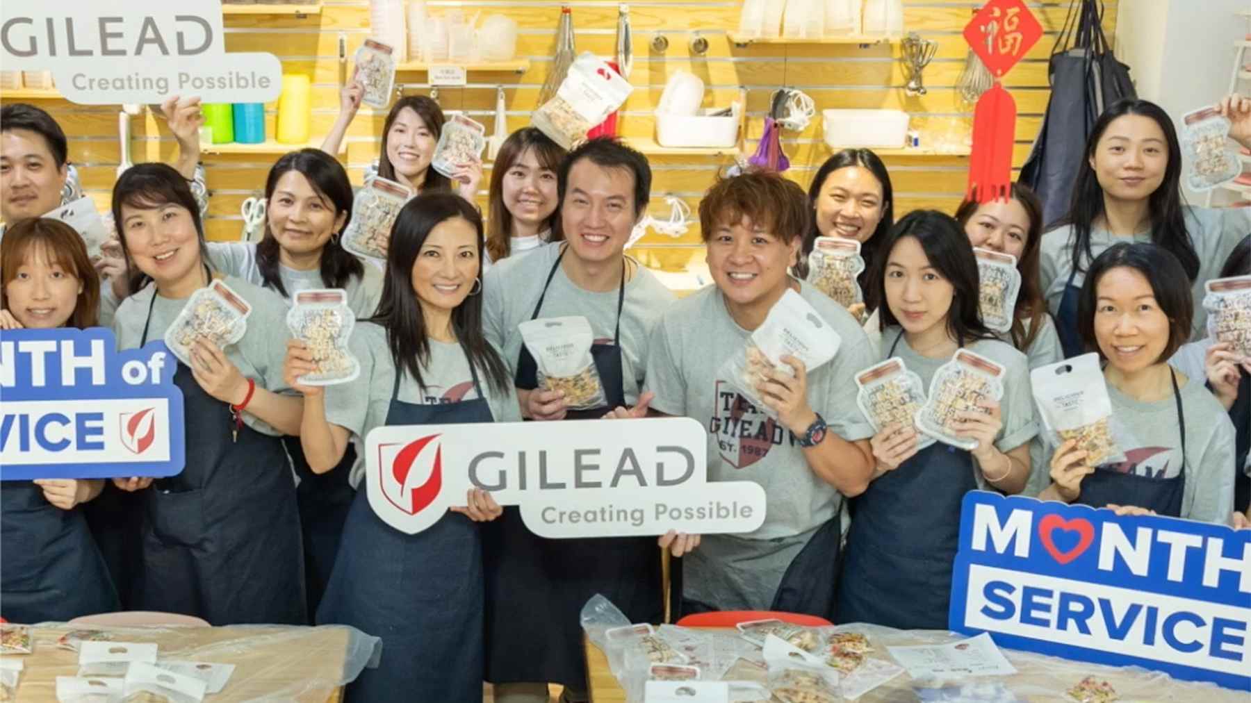 About twenty smiling Gilead volunteers holding Gilead and Month of Service signs at a service event