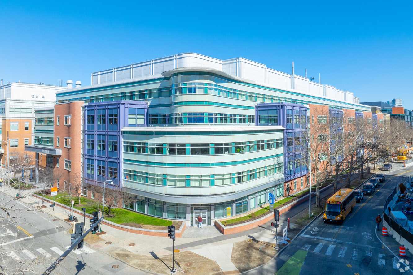 A curved glass and brick lab building on Binney Street in Cambridge, Massachusetts, under a clear sky