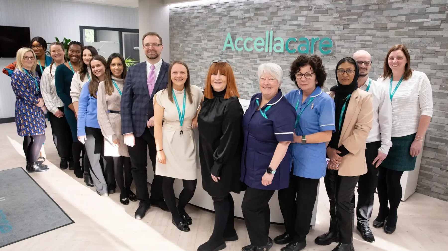 A large team of smiling Accellacare colleagues lined up in the lobby of their research site