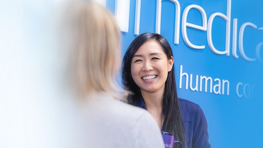 An ICU Medical colleague laughing with a coworker in front of the blue ICU Medical human connections wall