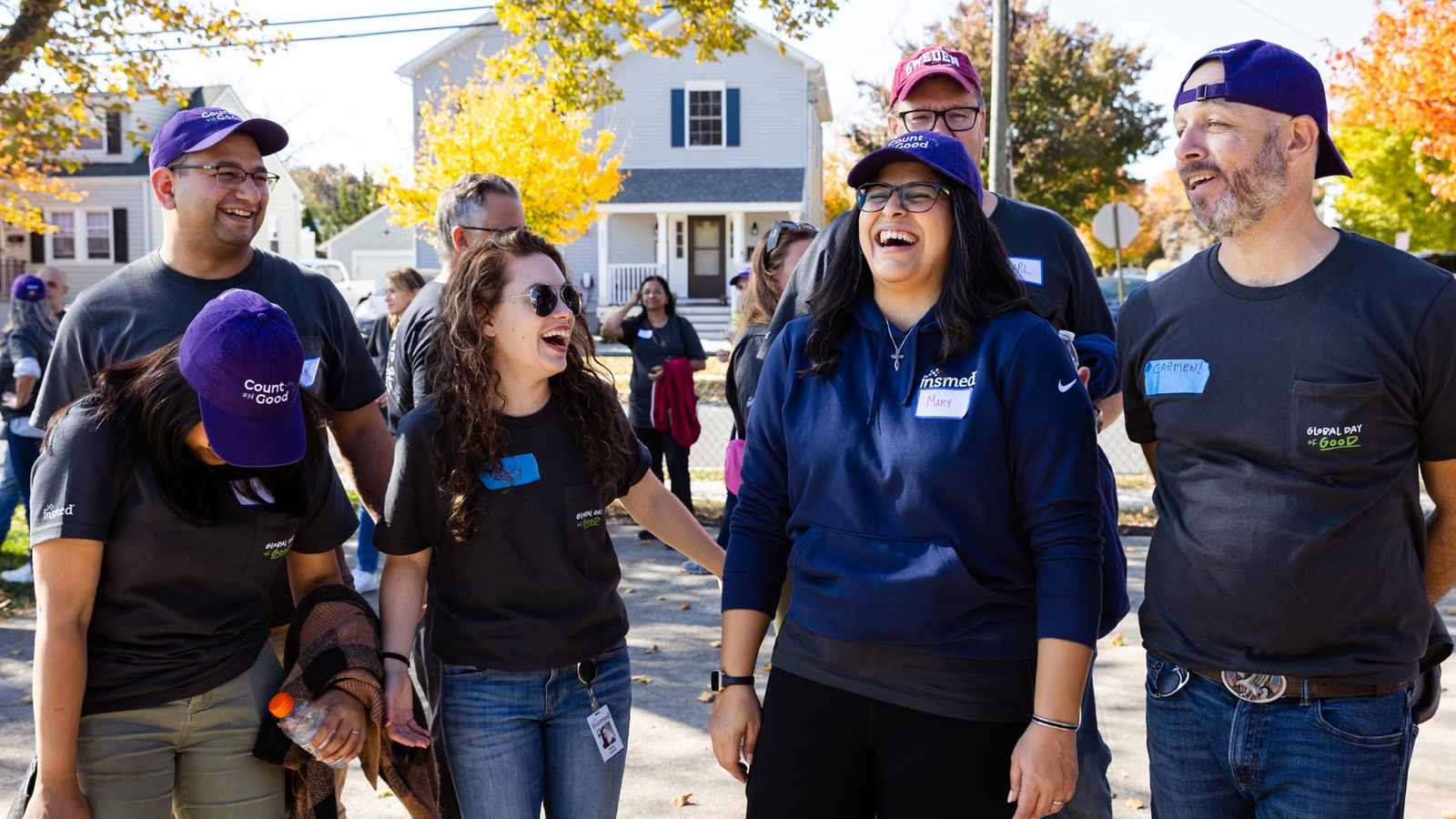 Insmed colleagues in Global Day of Good shirts and caps laughing together on a sunny autumn street