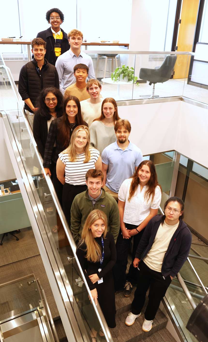Inspire's 2025 intern class standing together on an office stairwell, smiling up at the camera
