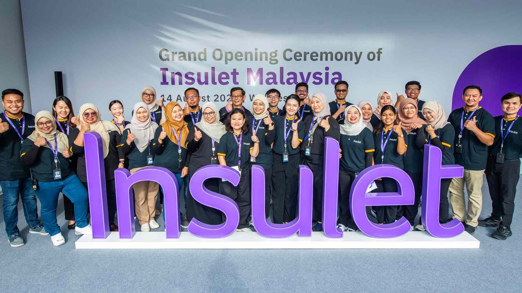 Dozens of smiling Insulet colleagues behind giant purple Insulet letters at the opening of Insulet Malaysia