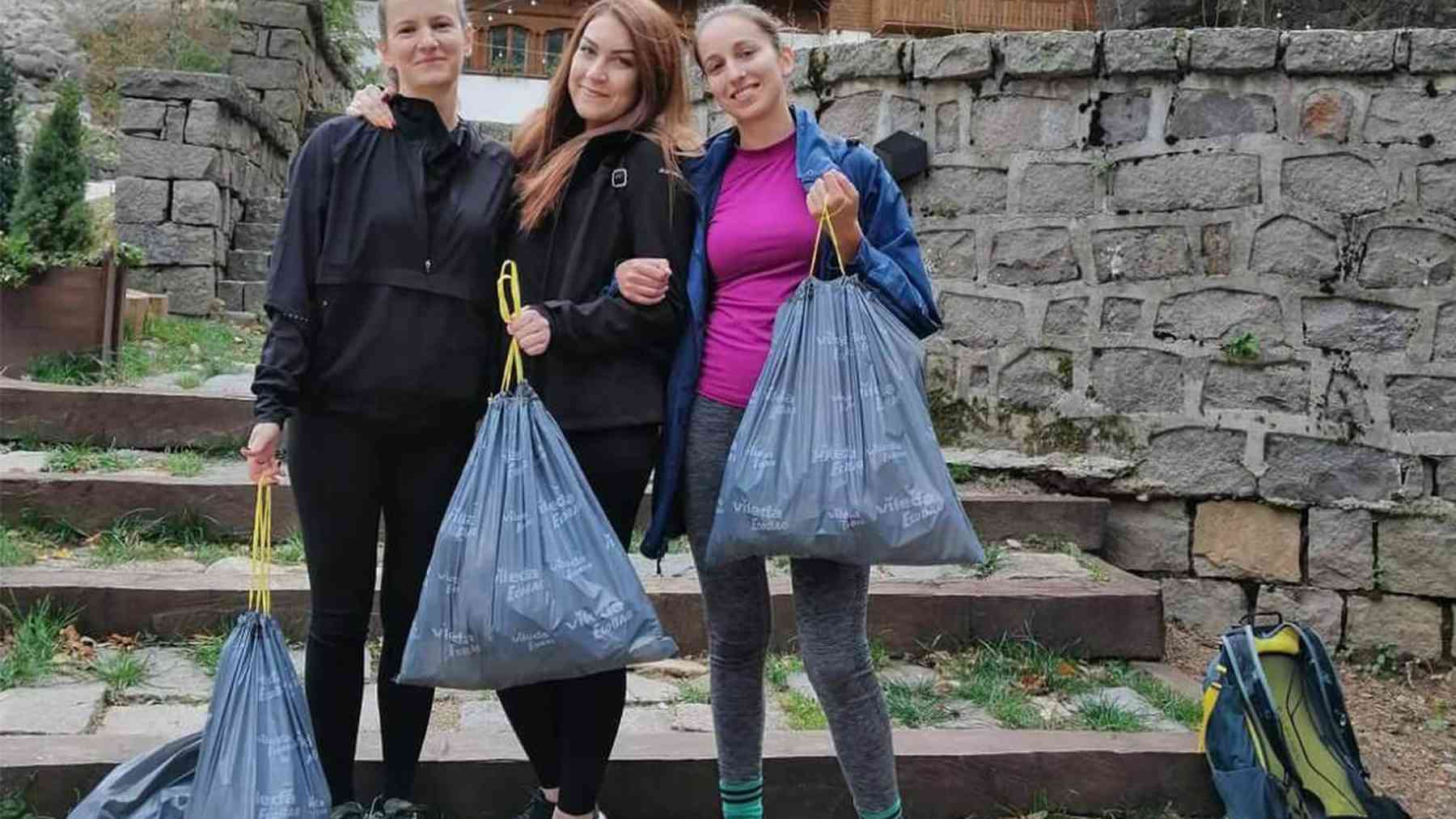 Three smiling IQVIA colleagues from Bulgaria holding full litter bags after a park clean-up