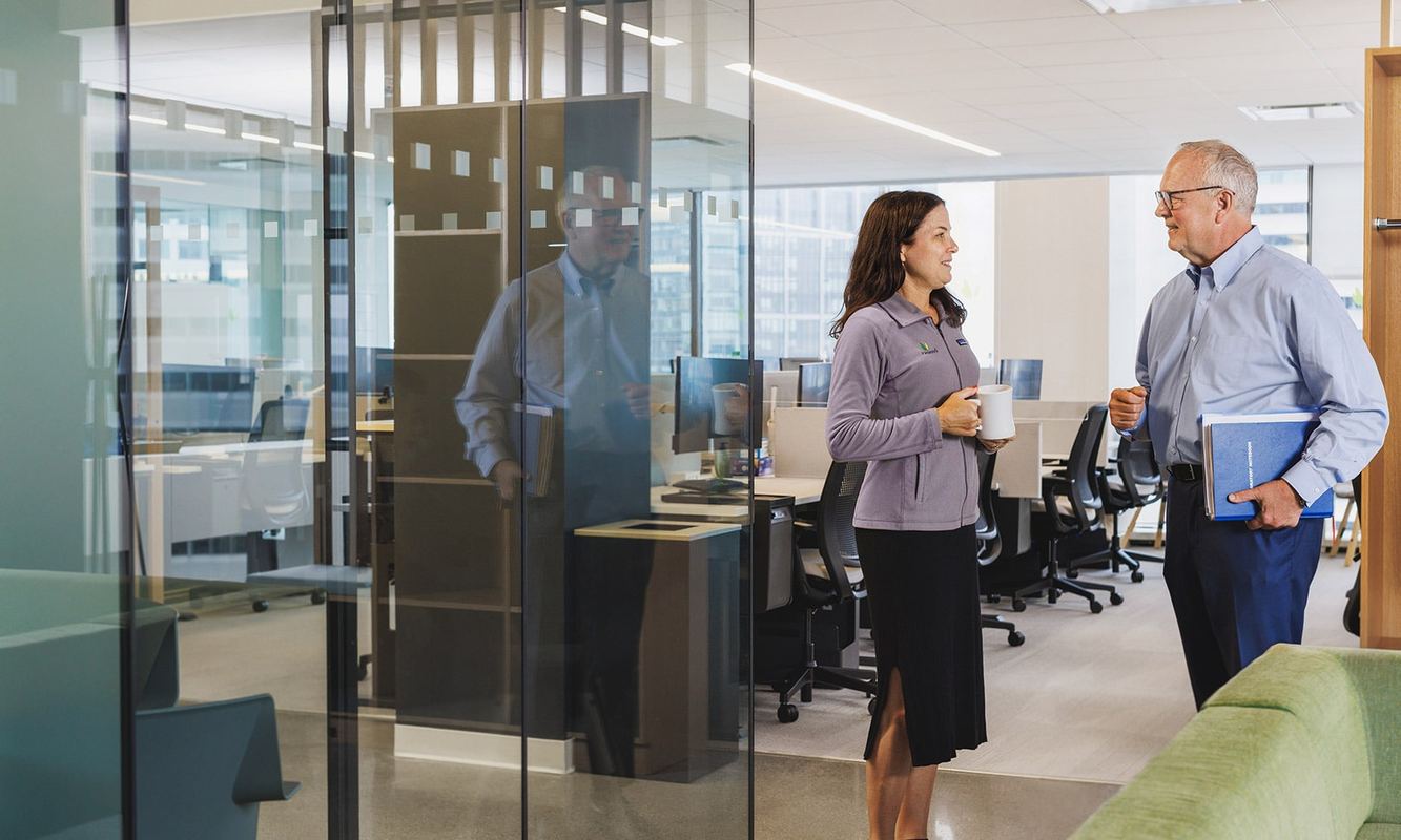 Two Ironwood colleagues talking over coffee in a bright, glass-walled office