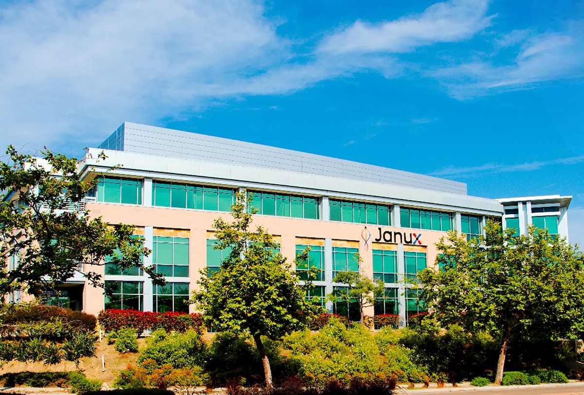 The Janux building with the Janux name on its facade behind flowering shrubs and trees