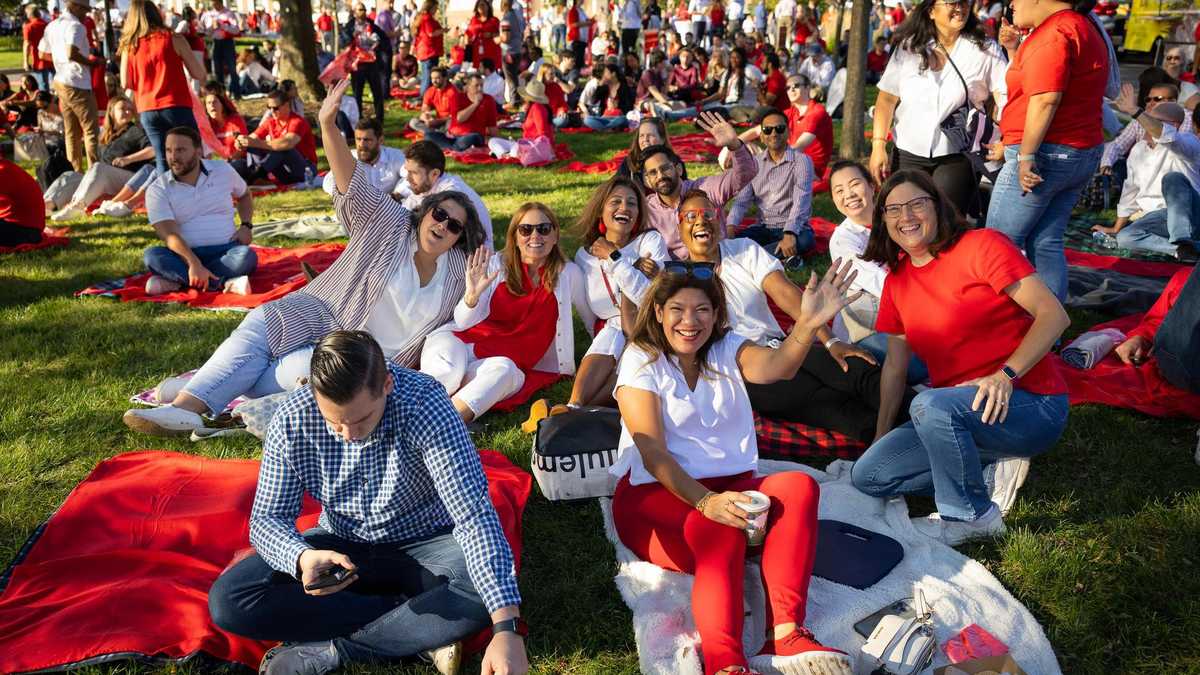 Smiling Johnson & Johnson employees waving from red picnic blankets on the lawn at J&J Day