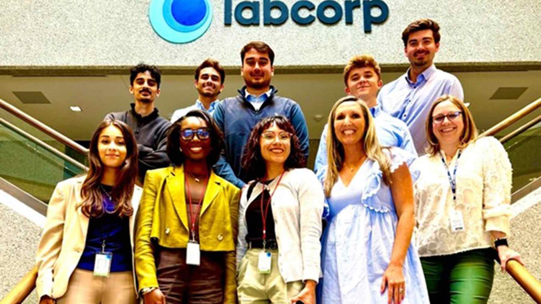 A smiling group of Labcorp interns and colleagues on a staircase beneath the Labcorp sign