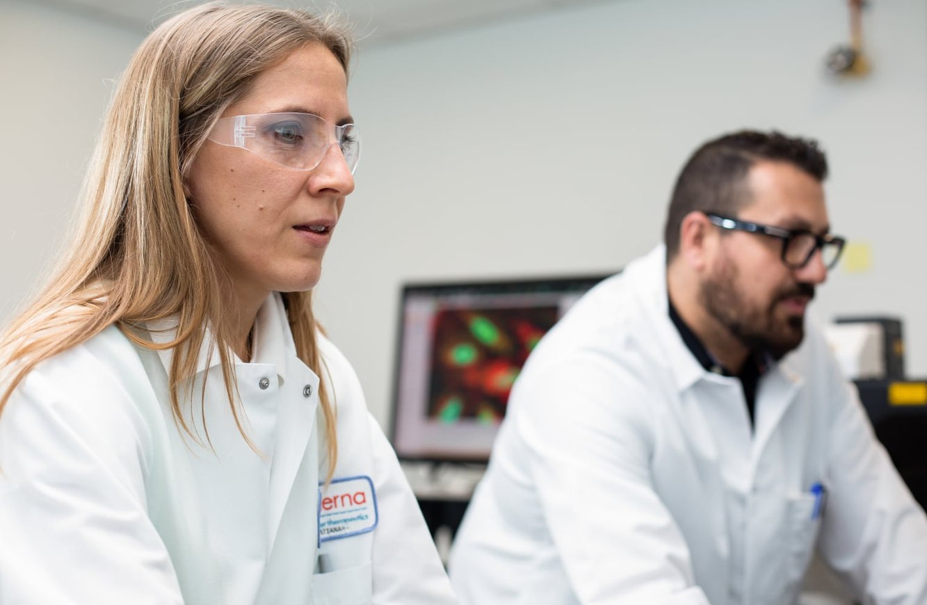 Two Moderna scientists in lab coats and safety glasses working at a lab bench