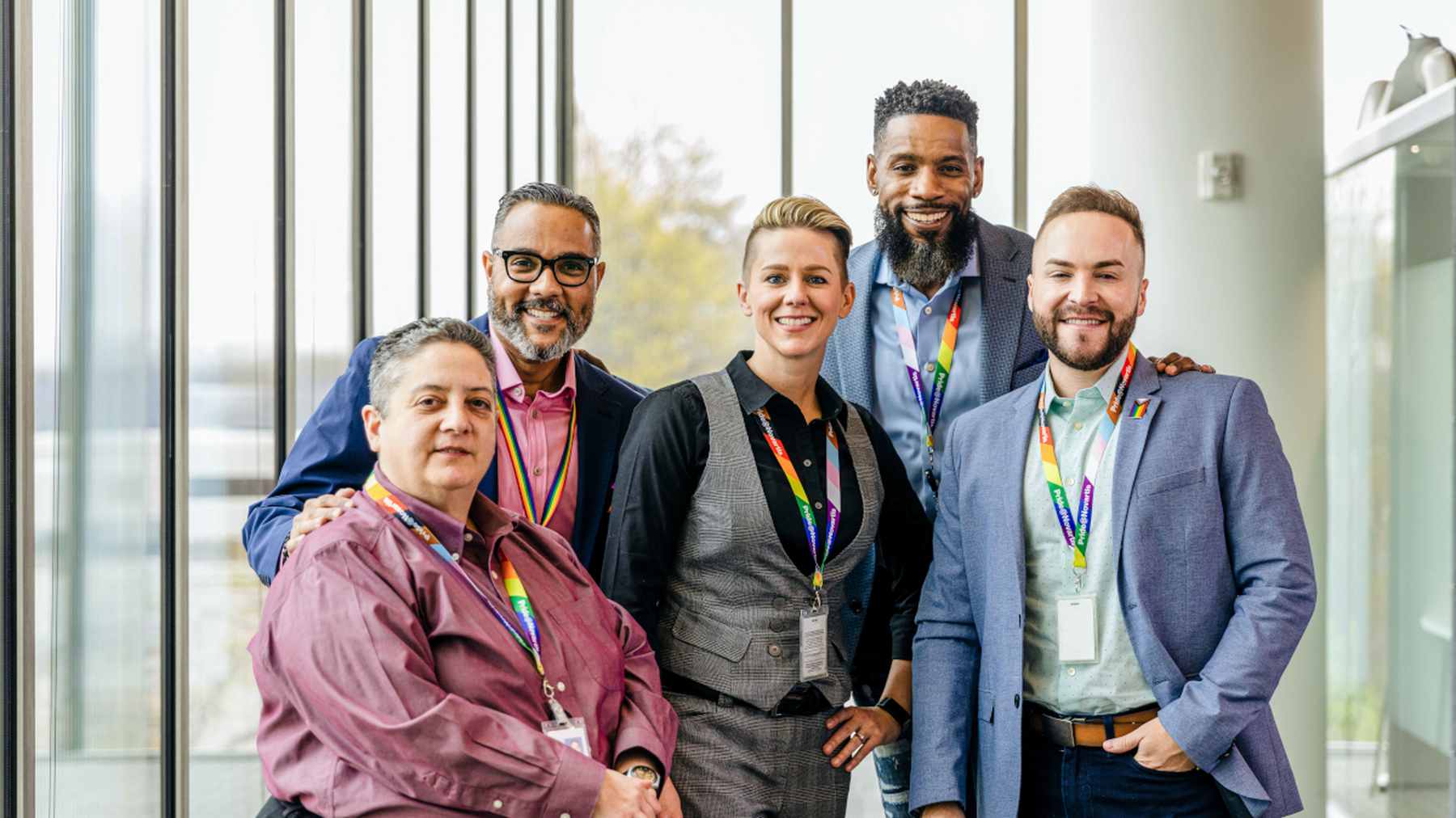 Five smiling Novartis colleagues wearing rainbow lanyards standing together to celebrate Pride