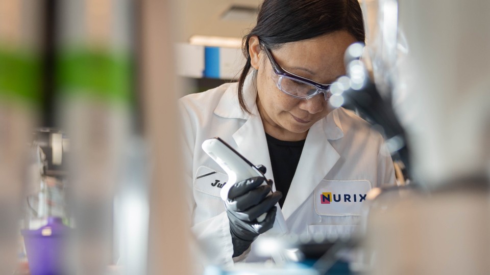 A Nurix scientist in safety glasses and a Nurix lab coat working at a lab bench