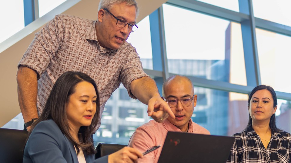 Four Nurix colleagues gathered around a laptop as one points to the screen in a sunlit office