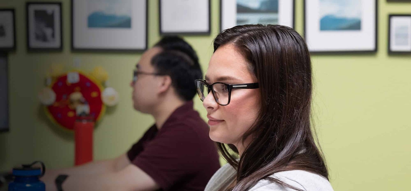 Two Orca Bio colleagues working at their desks in an office with framed landscape photos on a green wall