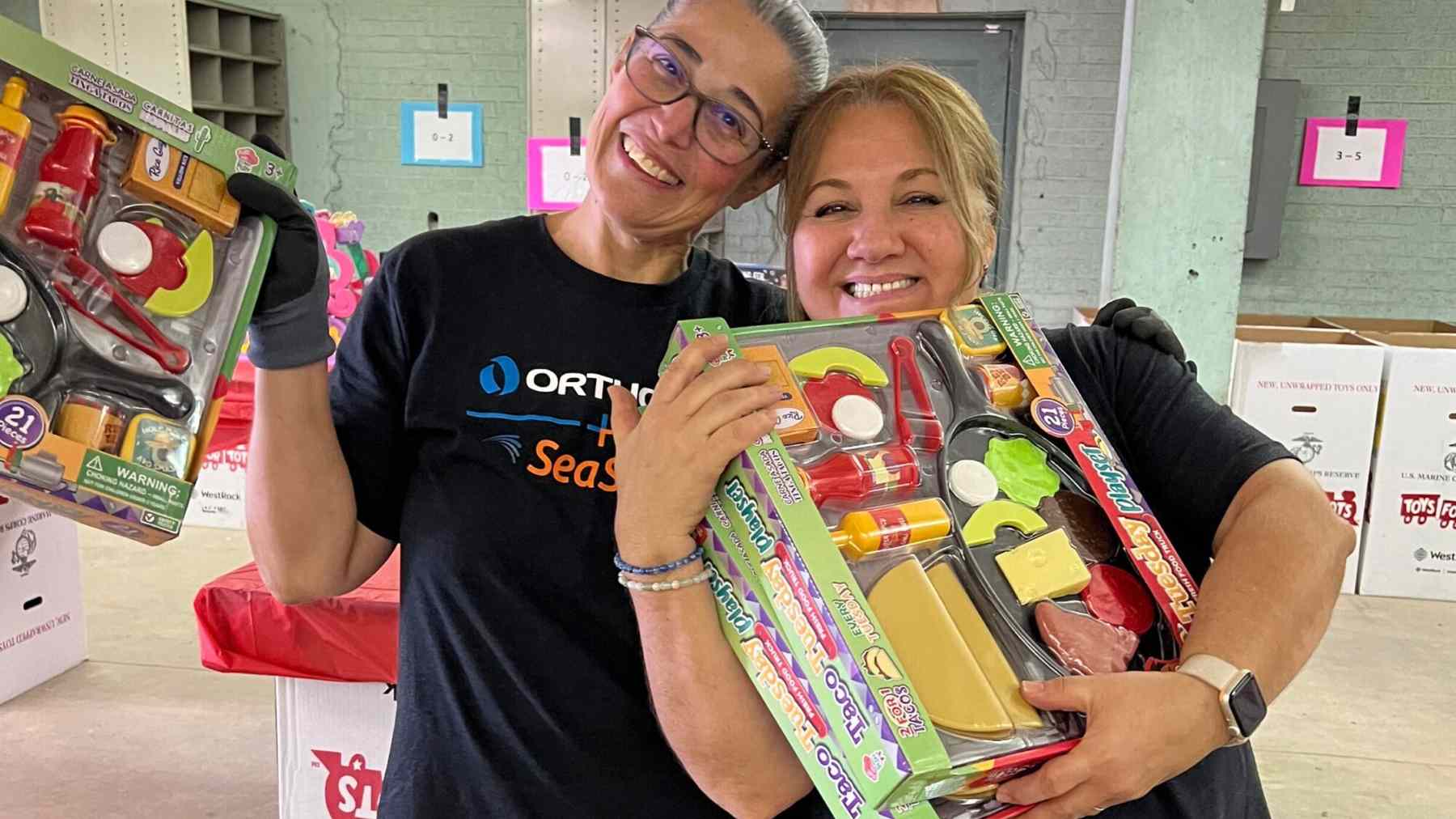 Two smiling Orthofix colleagues holding donated supplies at a community activity