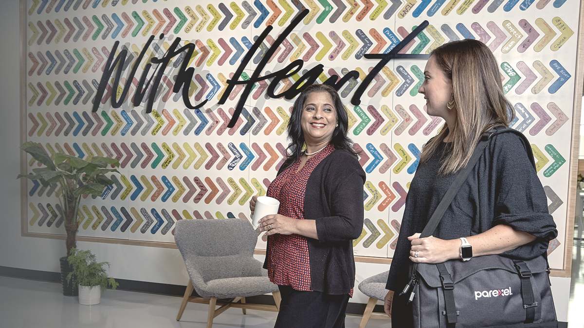 Two Parexel colleagues talking and smiling as they walk past the colorful With Heart wall in the office