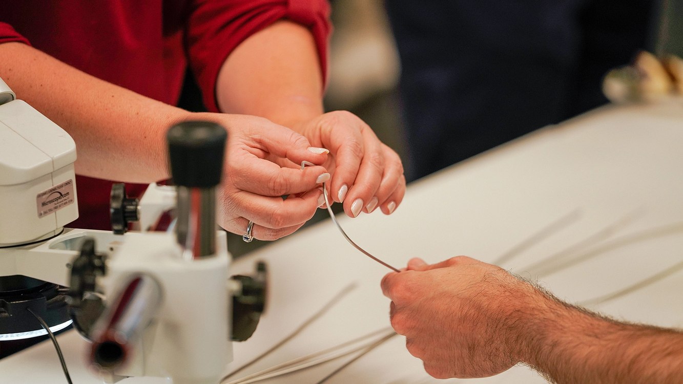 Penumbra engineers' hands threading a fine catheter wire beside a microscope at an R&D open house