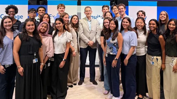 About thirty smiling young Pfizer colleagues posed together with a senior leader at an event