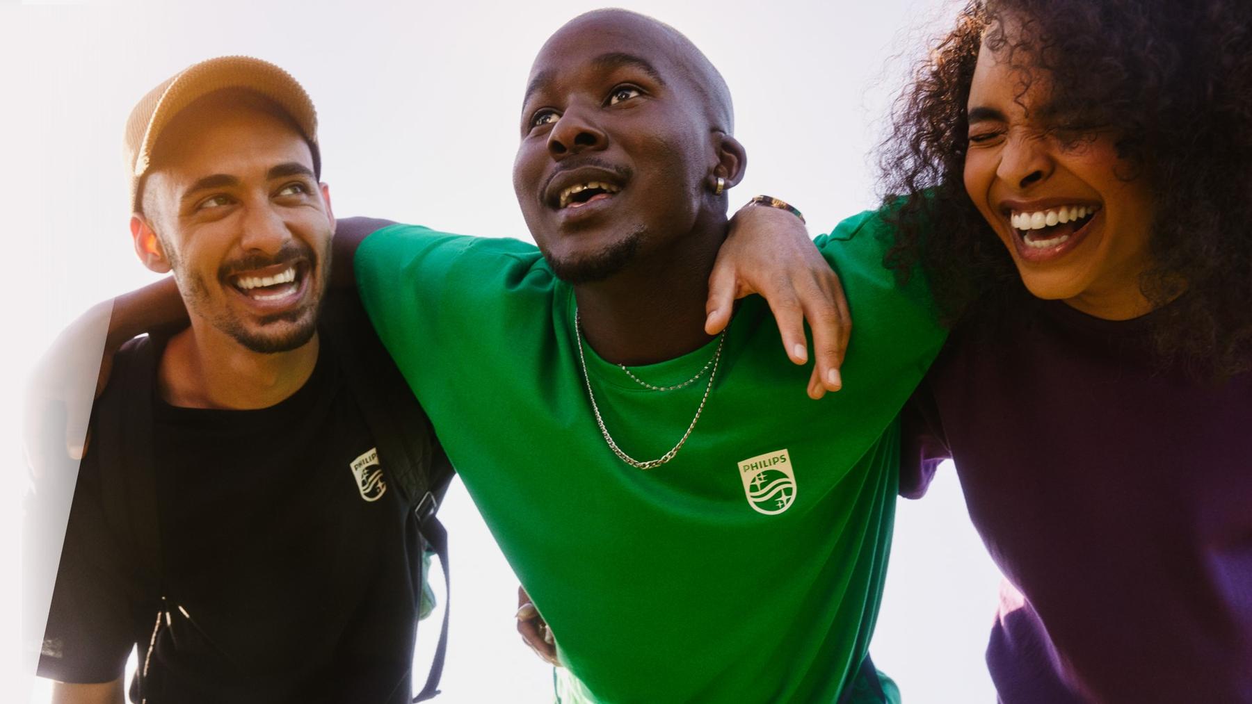 Three laughing Philips colleagues in Philips-branded shirts with their arms around each other