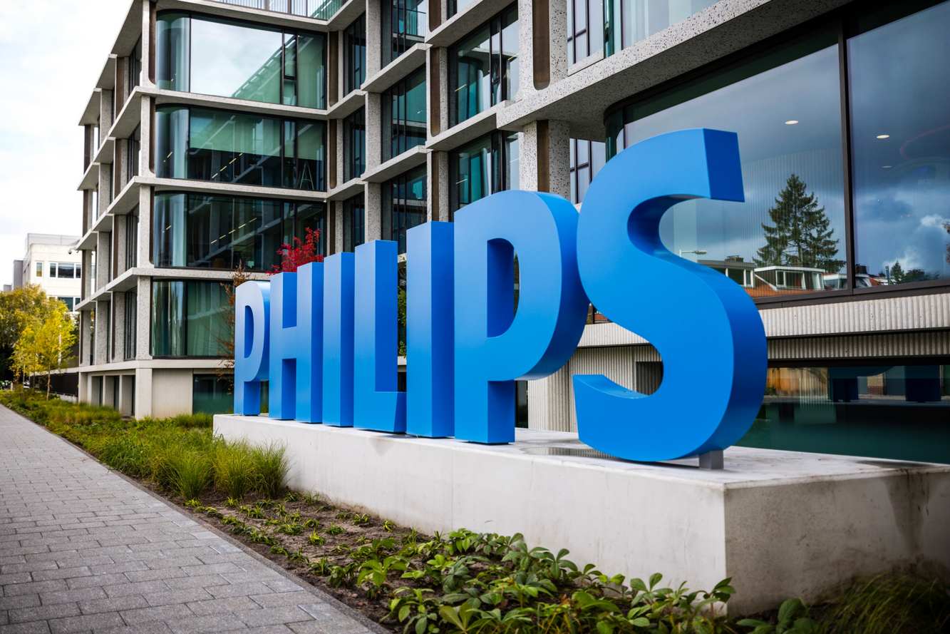 A large blue Philips sign in front of the glass Philips headquarters building