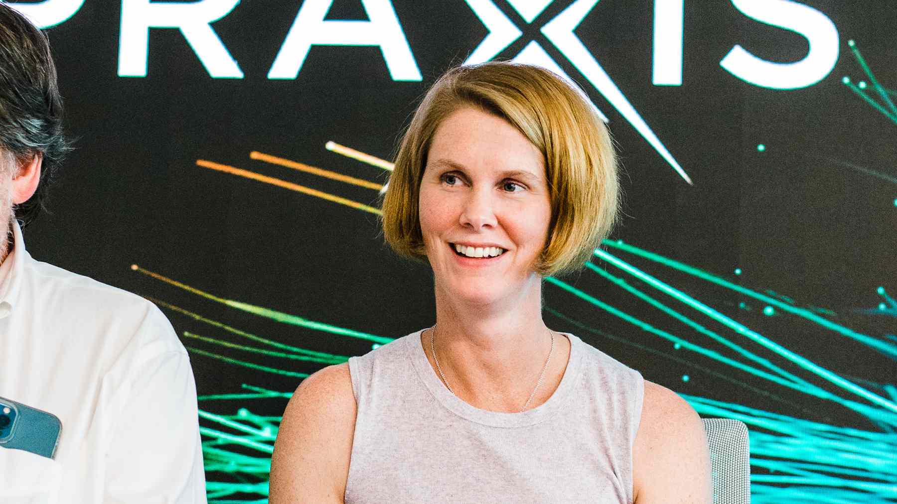 A smiling Praxis colleague seated on a panel in front of a backdrop with the Praxis logo