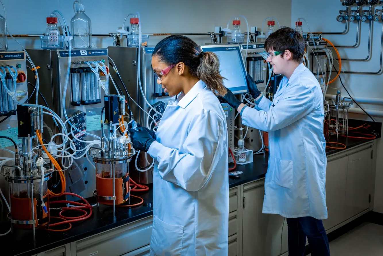 Two Regeneron scientists in lab coats working at bioreactors in a process development lab