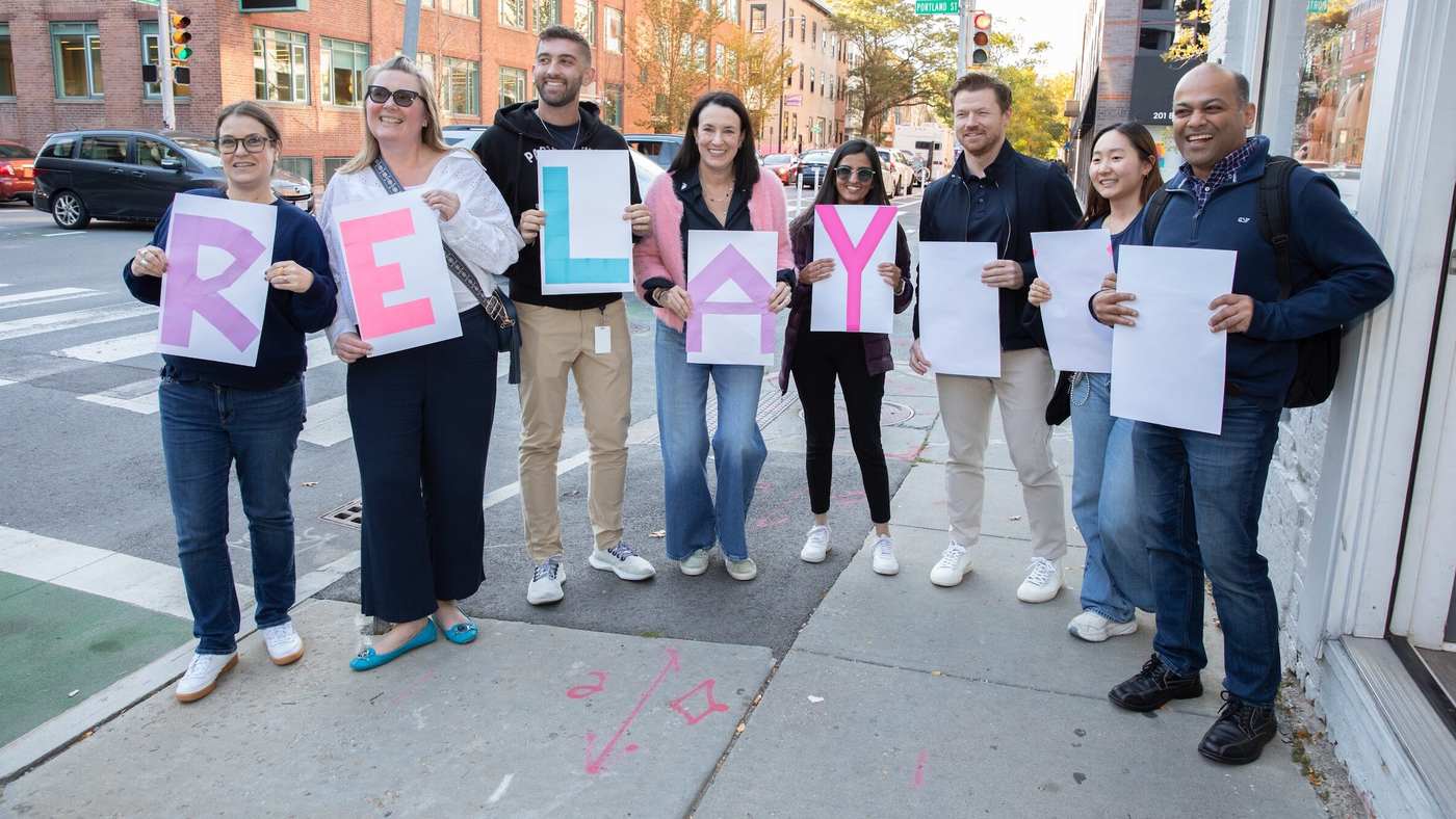 Ten smiling Relay Therapeutics colleagues on a Cambridge sidewalk holding letters that spell RELAY
