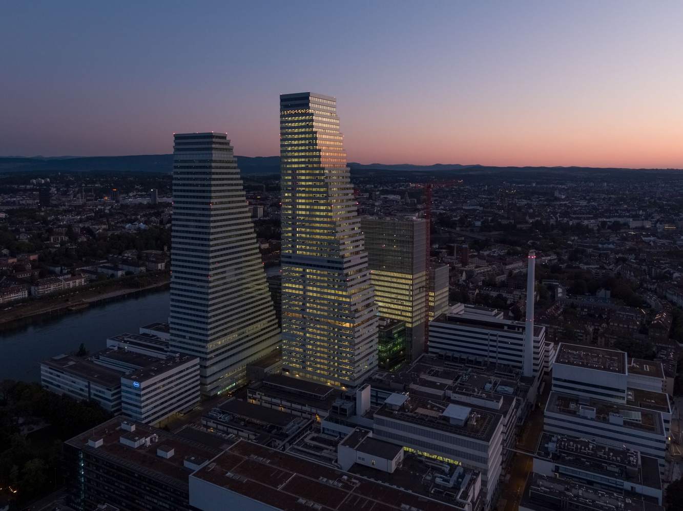 The two Roche towers above the Basel campus and the Rhine at dusk