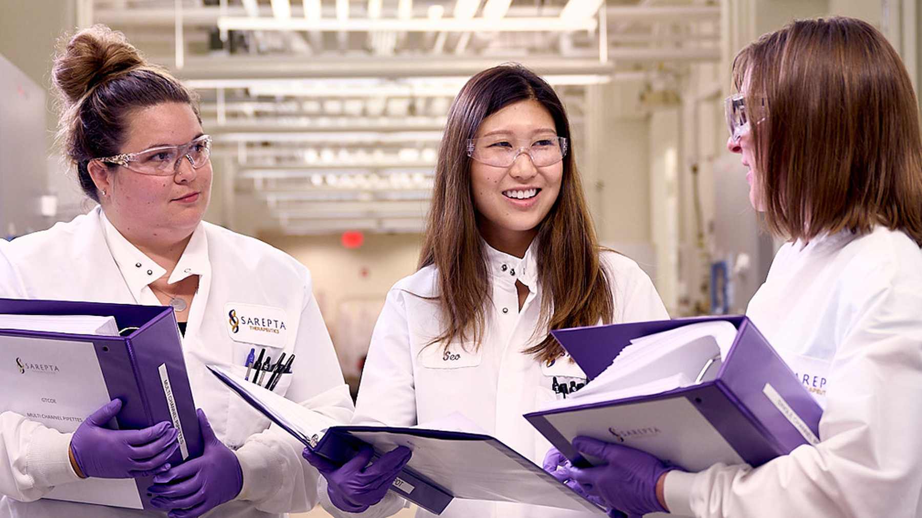 Three Sarepta colleagues smiling and discussing documents in the laboratory