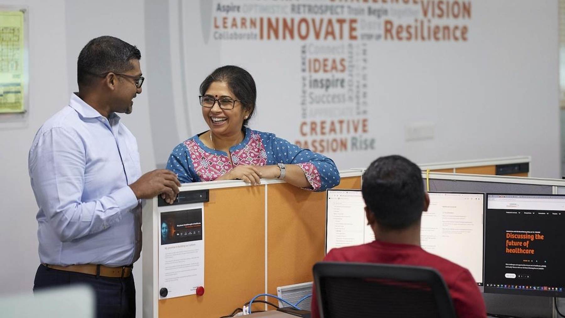 Siemens Healthineers colleagues laughing together across a desk partition in an office