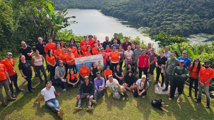 A large group of Smith+Nephew Costa Rica colleagues, many in orange shirts, posing on a hillside on a volunteering day