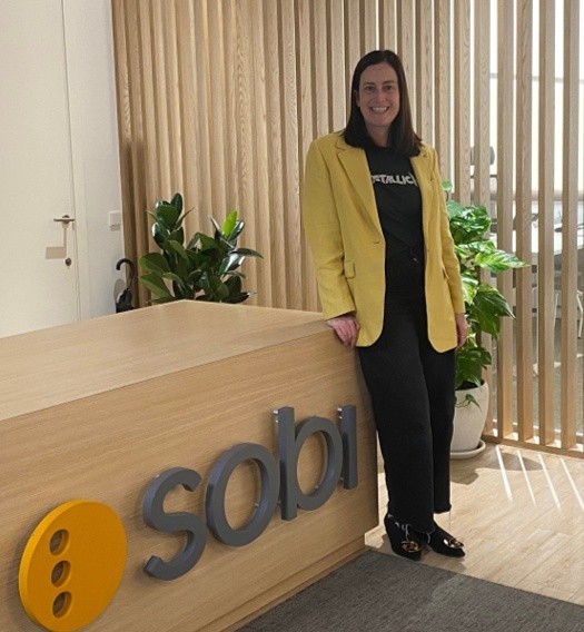 A smiling Sobi colleague in a yellow jacket leaning on the Sobi reception desk