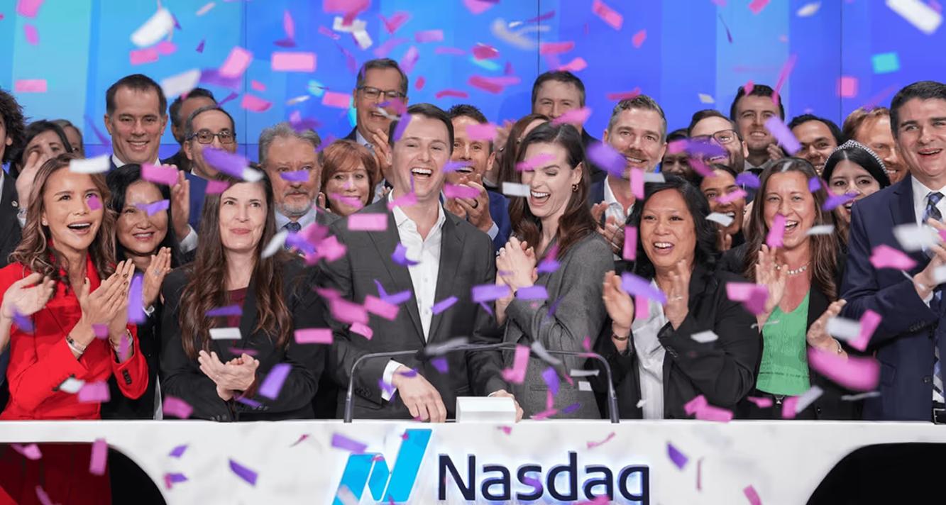Spyre colleagues cheering under falling confetti at the Nasdaq podium